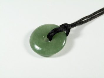 Zielony, okrągły jadeitowy wisiorek na czarnym sznurku, leżący na białym tle.