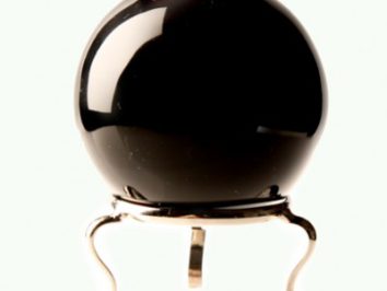Czarna kula wróżbiarska z obsydianu na metalowym stojaku na jasnym tle.