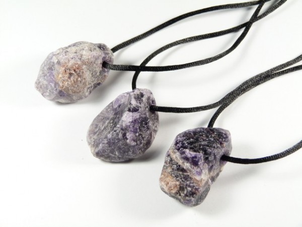 Trzy naszyjniki z surowych, fioletowych kamieni na czarnych sznurkach.