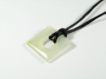 Kwadratowy wisiorek z jasnego kamienia na czarnym sznurku, widok z góry.