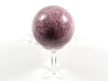 Fioletowa kula z kamienia na przezroczystej podstawce, na białym tle.