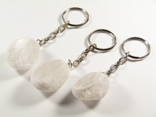 Trzy breloki z przezroczystymi kamieniami na metalowych łańcuszkach, leżące na białym tle.