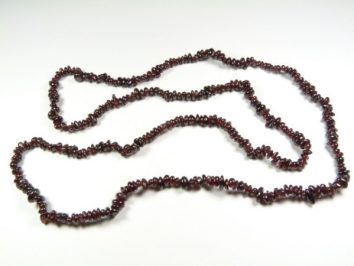 Naszyjnik z ciemnoczerwonych kamieni, ułożony na białym tle.