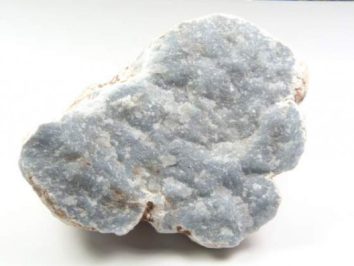 Szaro-niebieski minerał chalcedon na białym tle, widoczna jego ziarnista struktura.