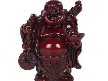 Ciemnoczerwona figurka uśmiechniętego Buddy trzymającego monety i sakiewkę, na białym tle.