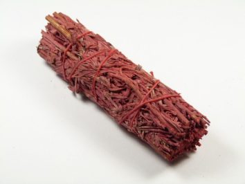 Czerwony pęczek suszonych ziół związany sznurkiem, leży na białym tle.