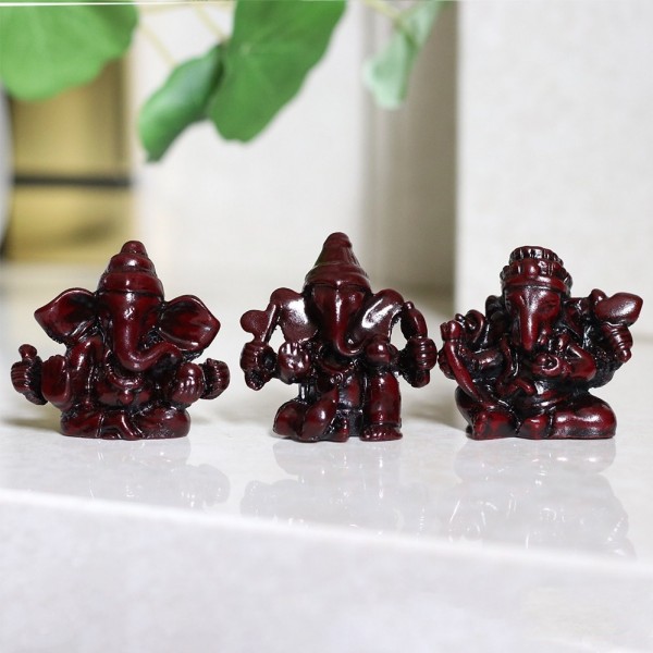 Trzy małe figurki Ganeszy ustawione w rzędzie na jasnej powierzchni.