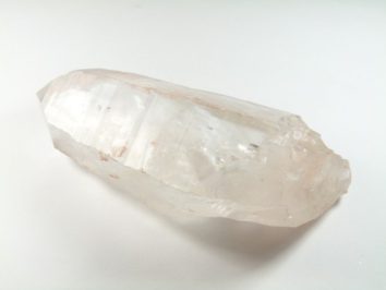 Przezroczysty kryształ kwarcu leży na białym tle.