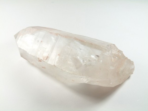 Przezroczysty kryształ kwarcu leży na białym tle.