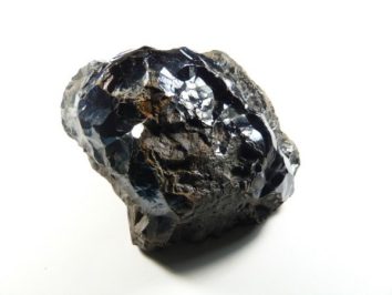 Hematyt - kamień naturalny, surowy, nieszlifowany. Czarny, błyszczący kamień hematyt na białym tle.