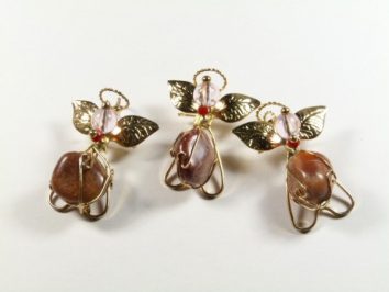 Trzy ozdoby w kształcie aniołków wykonane z drutu, kamieni i złotych liści na białym tle.