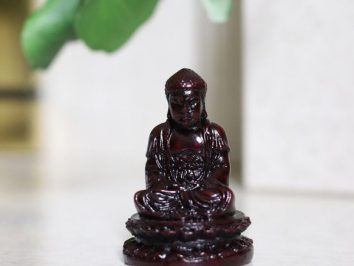 Mała figurka Buddy w pozycji siedzącej na białej powierzchni, w tle zielone liście.