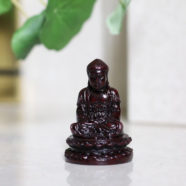 Mała figurka Buddy w pozycji siedzącej na białej powierzchni, w tle zielone liście.