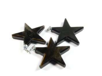 Trzy czarne, gwiaździste zawieszki leżą na białym tle.