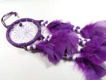 Fioletowy łapacz snów z piórkami i koralikami leży na białym tle.