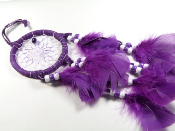 Fioletowy łapacz snów z piórkami i koralikami leży na białym tle.