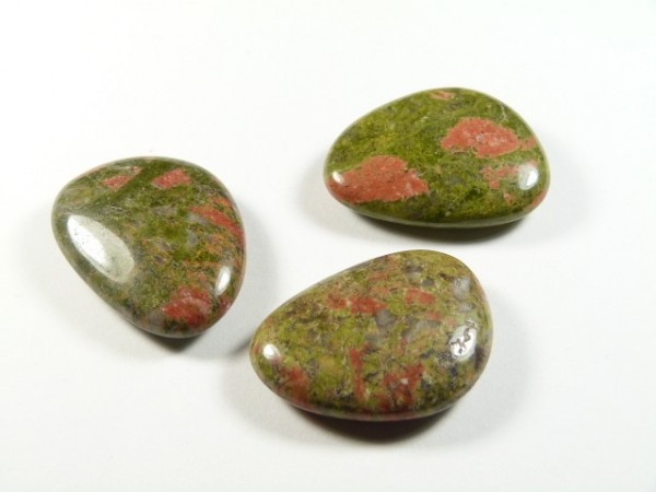 Unakit szlifowany - płaski kamień. Trzy polerowane kamienie unakitu o zielono-różowych barwach na białym tle.