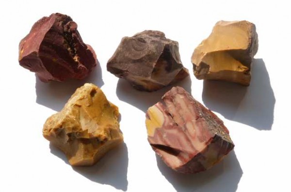 Mookait - kamień naturalny, surowy, nieszlifowany. Pięć surowych brył mookaitu w różnych odcieniach leży na białym tle.