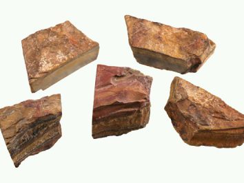 Pięć kawałków surowego krzemienia o brązowo-czerwonym kolorze leży na jasnym tle.