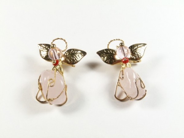 Dwa aniołki z różowego kamienia, ozdobione złotymi skrzydłami i aureolami, na białym tle.