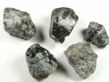 Pięć surowych, szaro-czarnych kamieni o niejednolitej strukturze na białym tle.