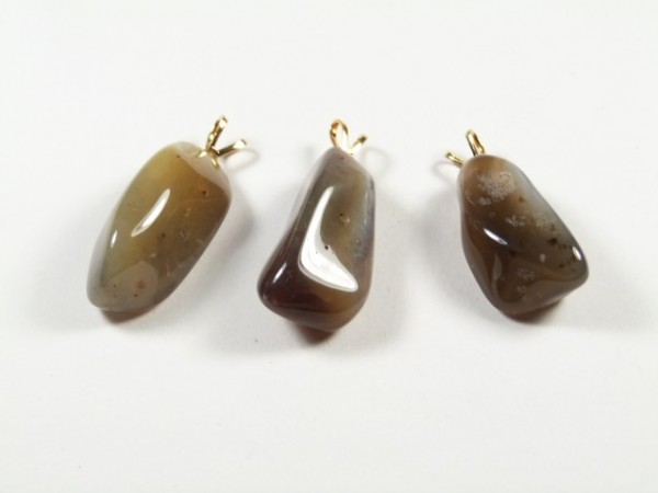Trzy polerowane wisiorki z agatu leżące na białym tle.