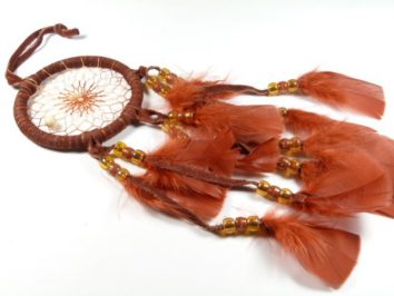 Brązowy łapacz snów z piórami i koralikami leży na białym tle.