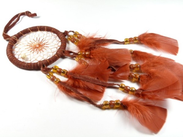 Brązowy łapacz snów z piórami i koralikami leży na białym tle.