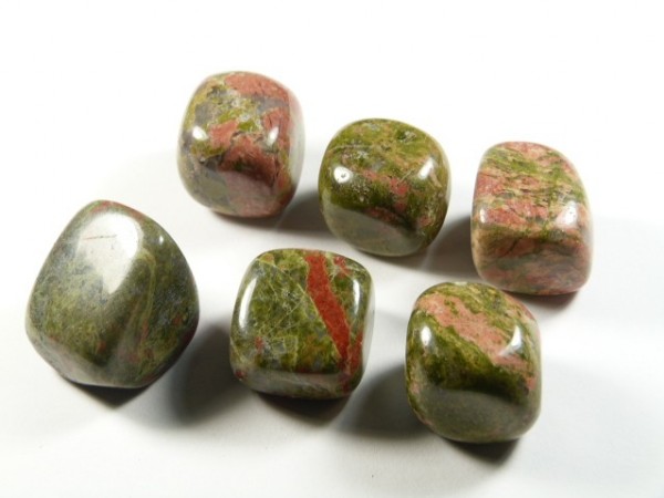 Unakit - kamień gładzony, polerowany, szlifowany i bębnowany w formie otoczaka. Sześć wypolerowanych kamieni unakitu z różowymi i zielonymi wzorami na białym tle.