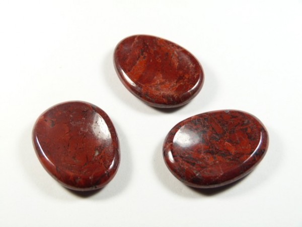 Jaspis brekcja płaski szlifowany. Trzy gładkie, czerwono-brązowe kamienie, leżące na białym tle.