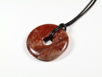 Okrągły wisior z czerwonego kamienia zawieszony na czarnym sznurku, na białym tle.