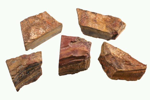 Pięć kawałków surowego krzemienia o brązowych i czerwonych odcieniach na białym tle.