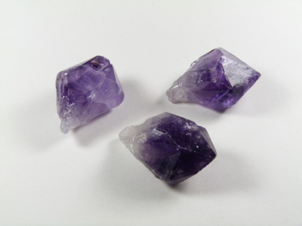 Trzy surowe kryształy ametystu na białym tle.