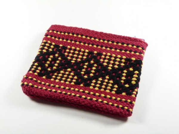 Czerwona, tkana portmonetka z żółtym i czarnym geometrycznym wzorem leży na białym tle.