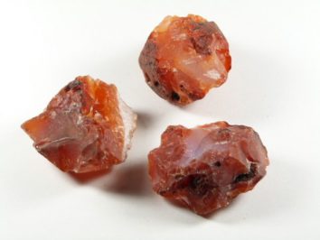 Trzy surowe bryłki karneolu leżące na białym tle.