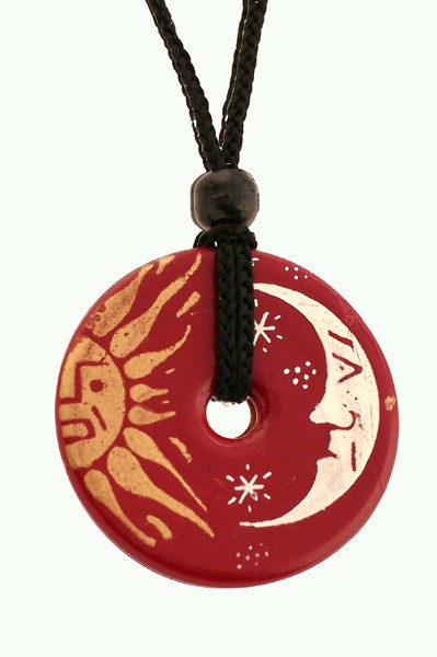 Czerwony okrągły wisiorek z motywem słońca i księżyca, zawieszony na czarnym sznurku.