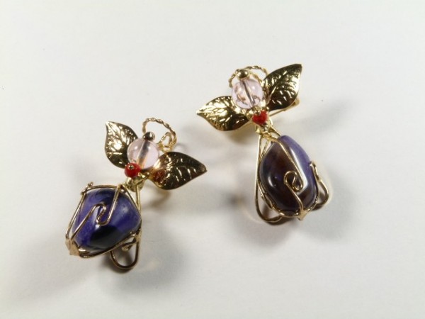 Dwa ozdobne aniołki z fioletowych kamieni i złotych elementów na białym tle.