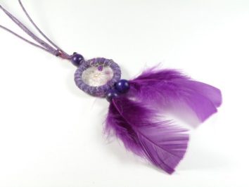 Fioletowy łapacz snów z piórami i koralikami, leżący na białym tle.