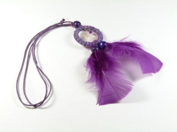Fioletowy łapacz snów z piórami i koralikami leży na białym tle.