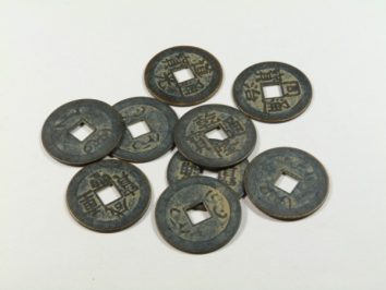 Osiem starych chińskich monet z kwadratowymi otworami leży na białym tle.