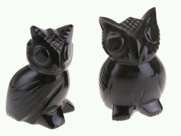 Dwie czarne figurki sów wykonane z połyskującego materiału na jasnym tle.