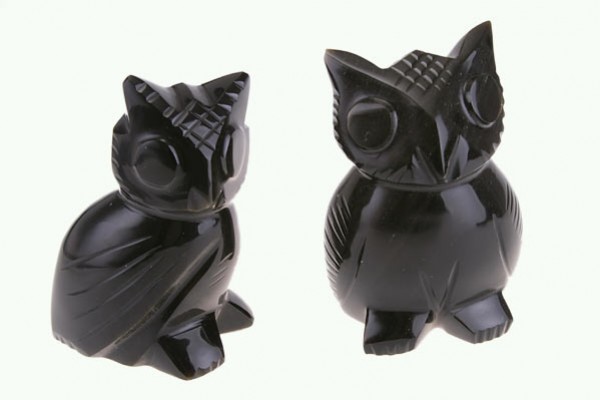 Dwie czarne figurki sów wykonane z połyskującego materiału na jasnym tle.