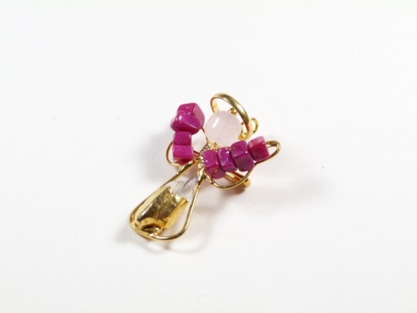 Złoty wisiorek w kształcie aniołka z różowymi i przezroczystymi koralikami na białym tle.