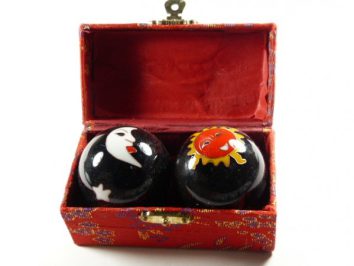 Dwie czarne kulki z motywem słońca i księżyca w ozdobnym czerwonym pudełku.
