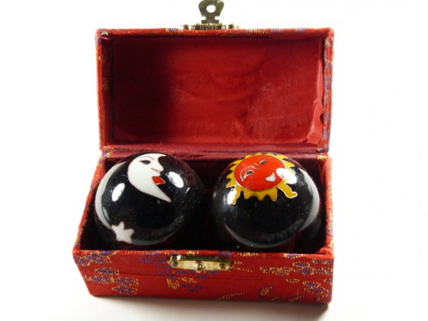 Dwie czarne kulki z motywem słońca i księżyca w ozdobnym czerwonym pudełku.