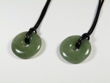 Dwa zielone, okrągłe wisiorki z jadeitu na czarnych sznurkach leżą na białym tle.