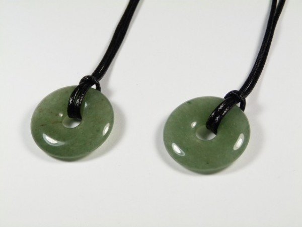 Dwa zielone, okrągłe wisiorki z jadeitu na czarnych sznurkach leżą na białym tle.