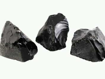 Trzy kawałki czarnego obsydianu na jasnym tle.
