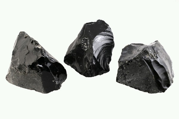Trzy kawałki czarnego obsydianu na jasnym tle.