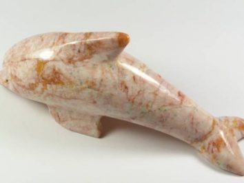 Rzeźba delfina wykonana z różowego marmuru, leżąca na białym tle.